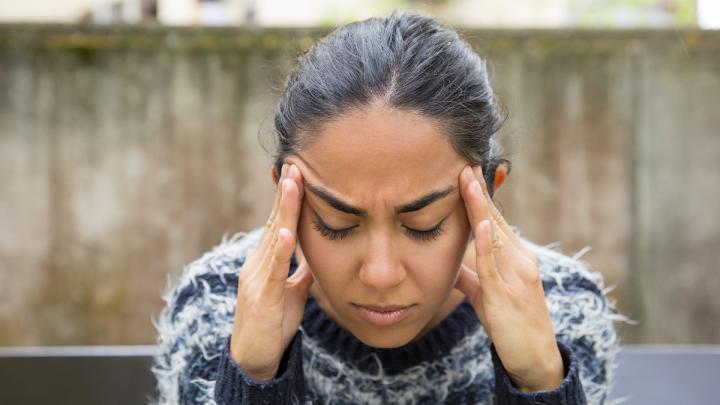 A girl sitting with her hands on her temples like she has a headache.