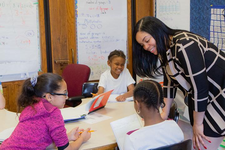 Female teacher interacting with K-12 students in a classroom.